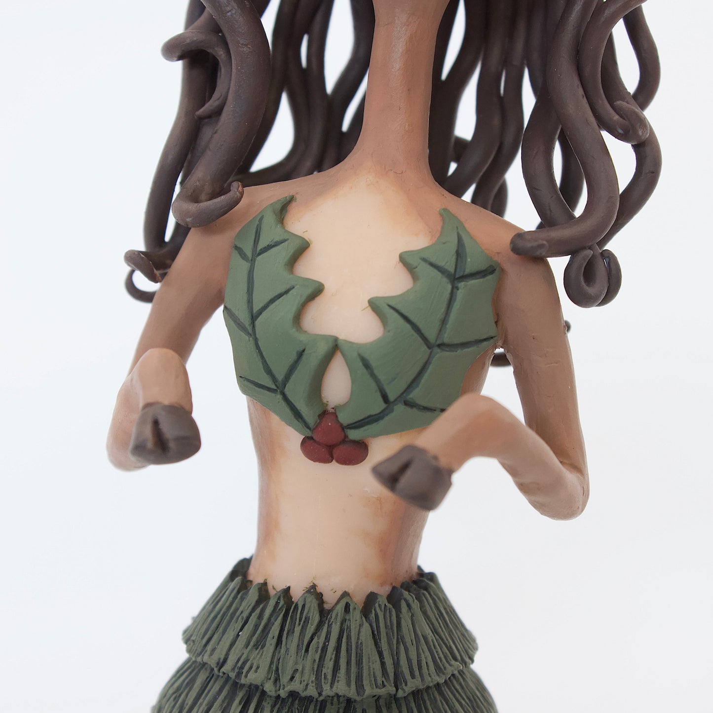 A polymer clay sculpture of a reindeer human hybrid, featuring antlers, a christmas tree skirt, and holly berries and leaves for the top. Also with the iconic Rudolph red nose and deer like ears and hooves.