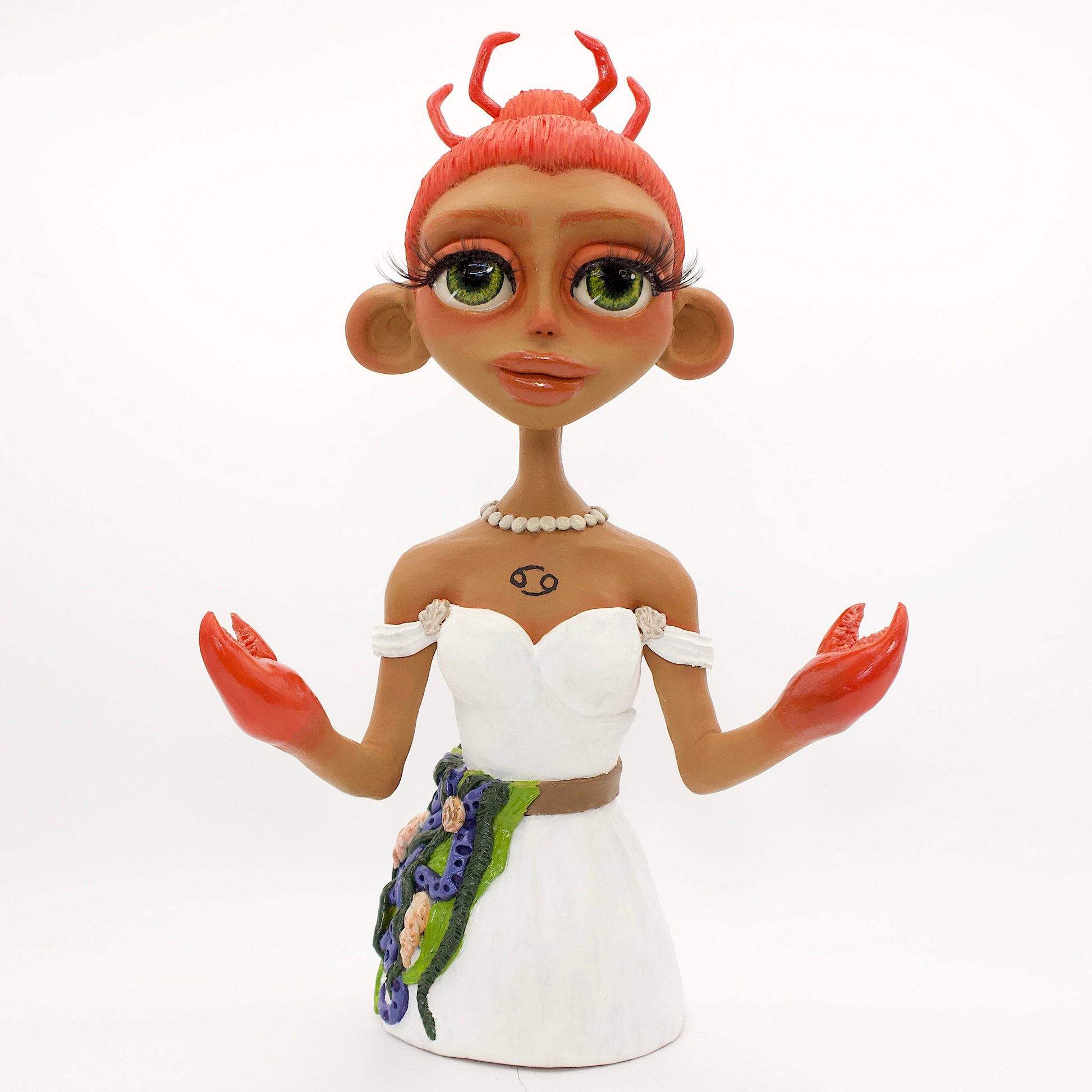 A polymer clay sculpture of the Cancer zodiac personified as a woman, featuring a seaweed belt, crab claws for hands and crab legs in her hair, she is wearing a white dress decorated with sea shells.
