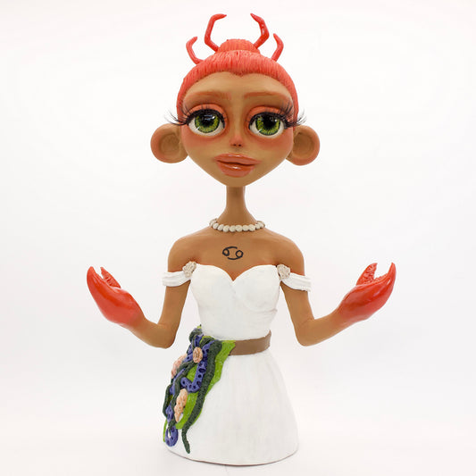 A polymer clay sculpture of the Cancer zodiac personified as a woman, featuring a seaweed belt, crab claws for hands and crab legs in her hair, she is wearing a white dress decorated with sea shells.