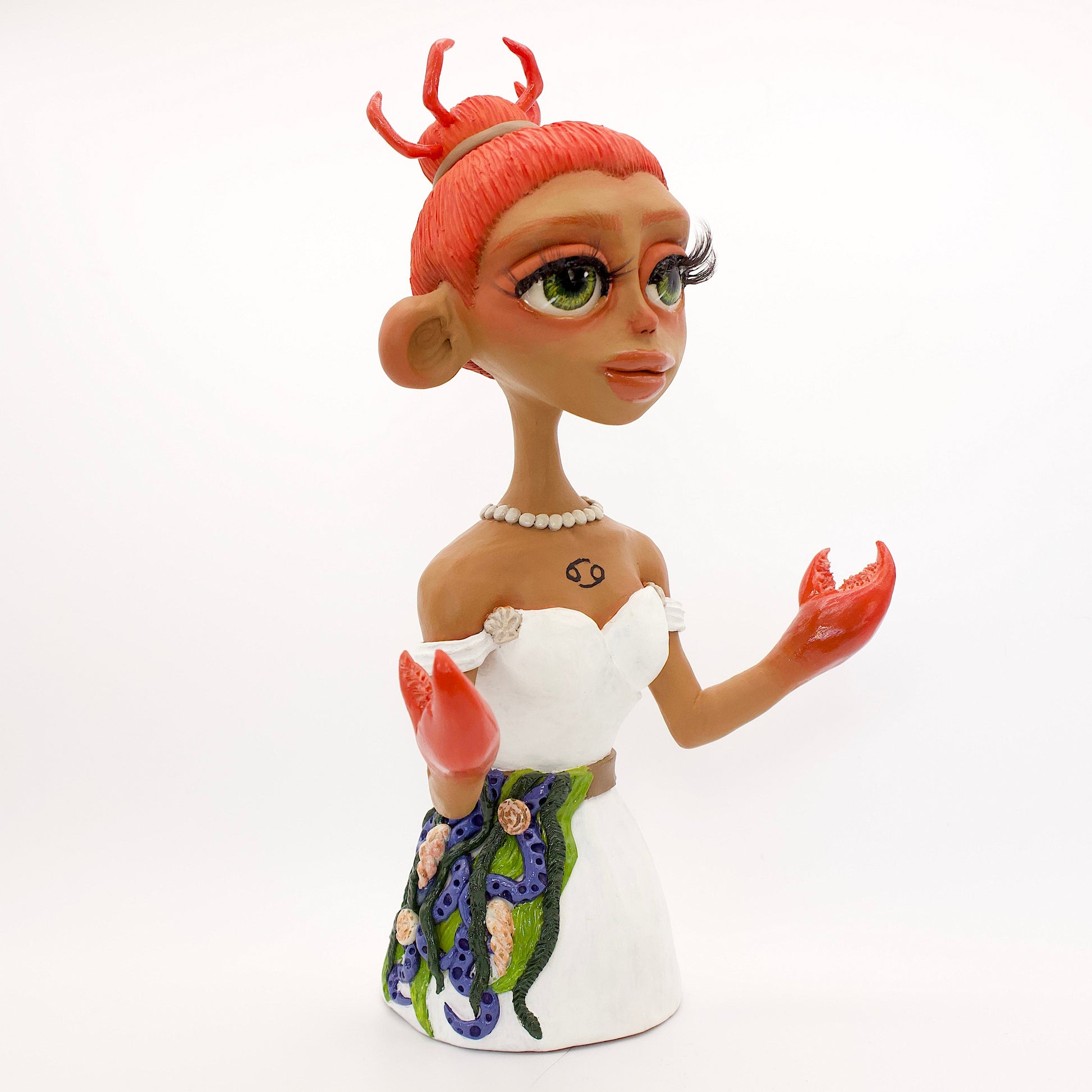 A polymer clay sculpture of the Cancer zodiac personified as a woman, featuring a seaweed belt, crab claws for hands and crab legs in her hair, she is wearing a white dress decorated with sea shells.