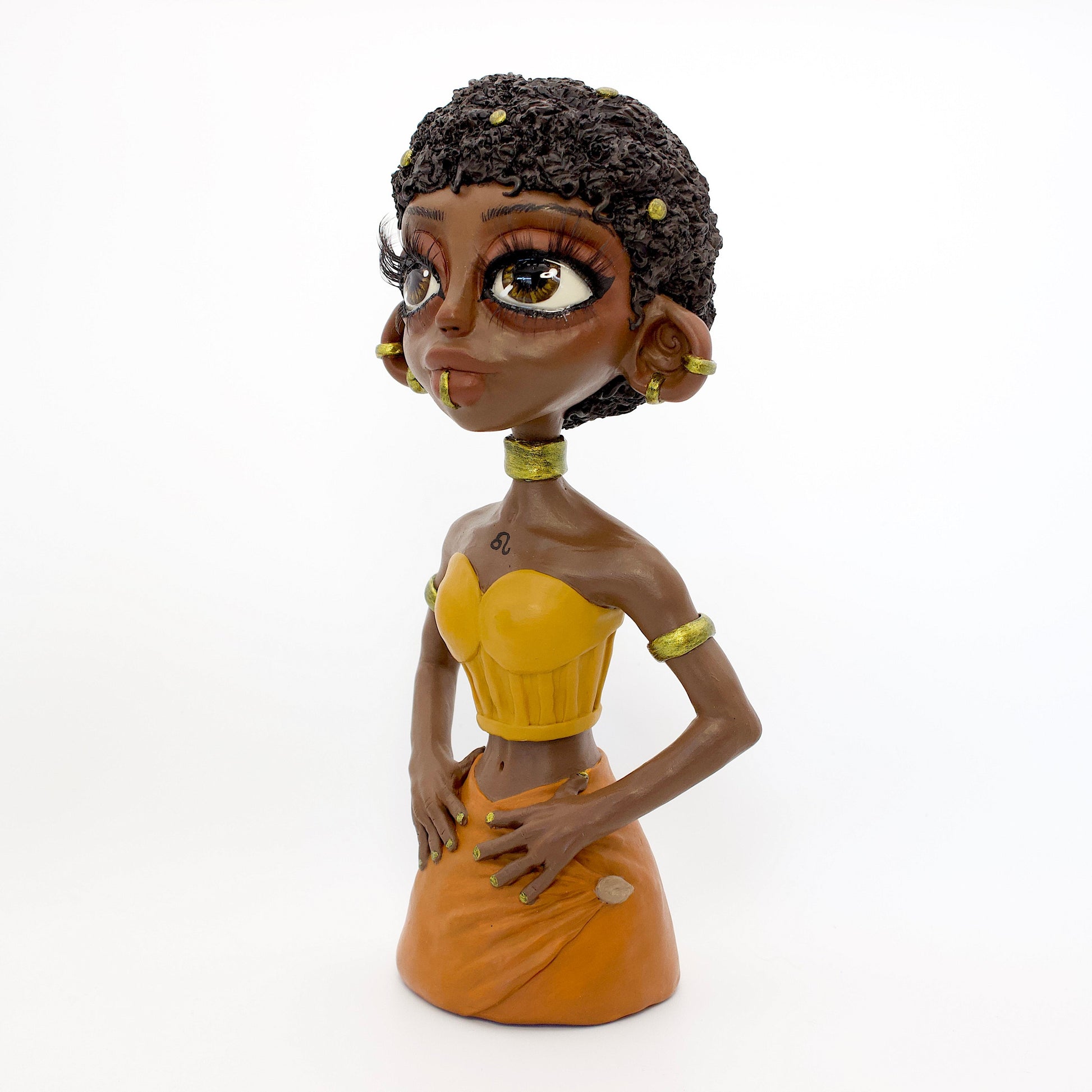 A polymer clay sculpture of the Leo zodiac personified as a woman, featuring yellow, orange and gold tones, and a mane-like afro hairstyle.