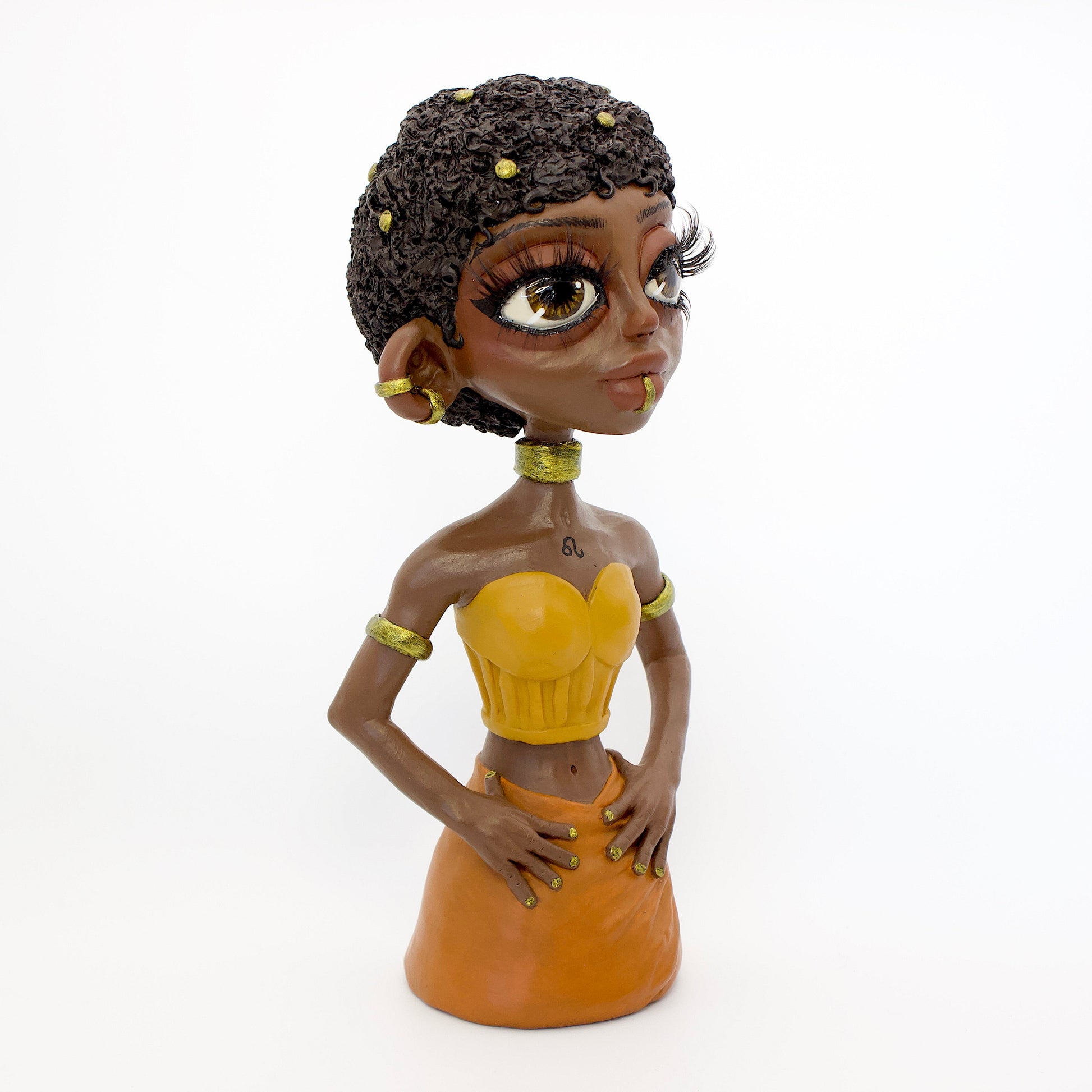 A polymer clay sculpture of the Leo zodiac personified as a woman, featuring yellow, orange and gold tones, and a mane-like afro hairstyle.