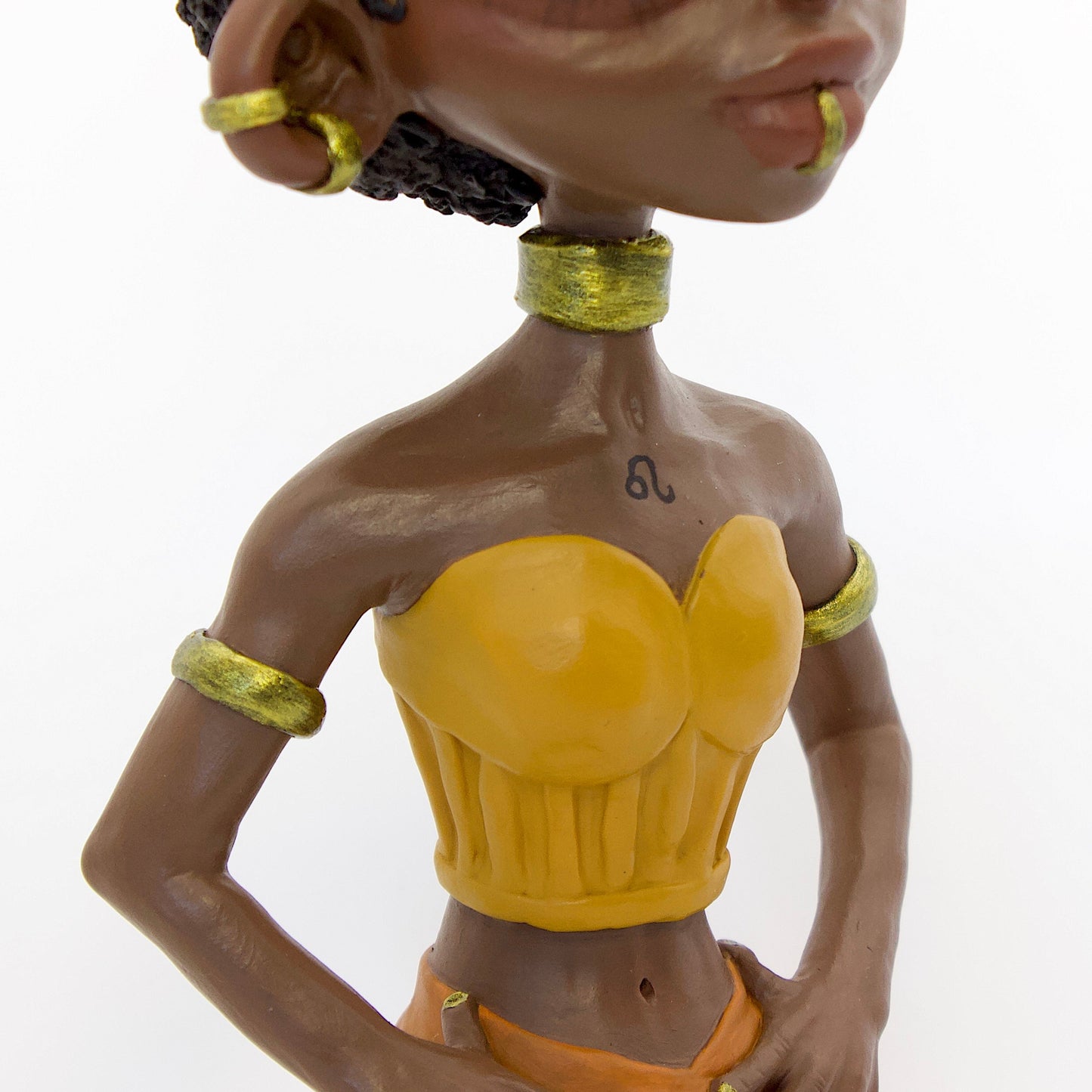 A polymer clay sculpture of the Leo zodiac personified as a woman, featuring yellow, orange and gold tones, and a mane-like afro hairstyle.