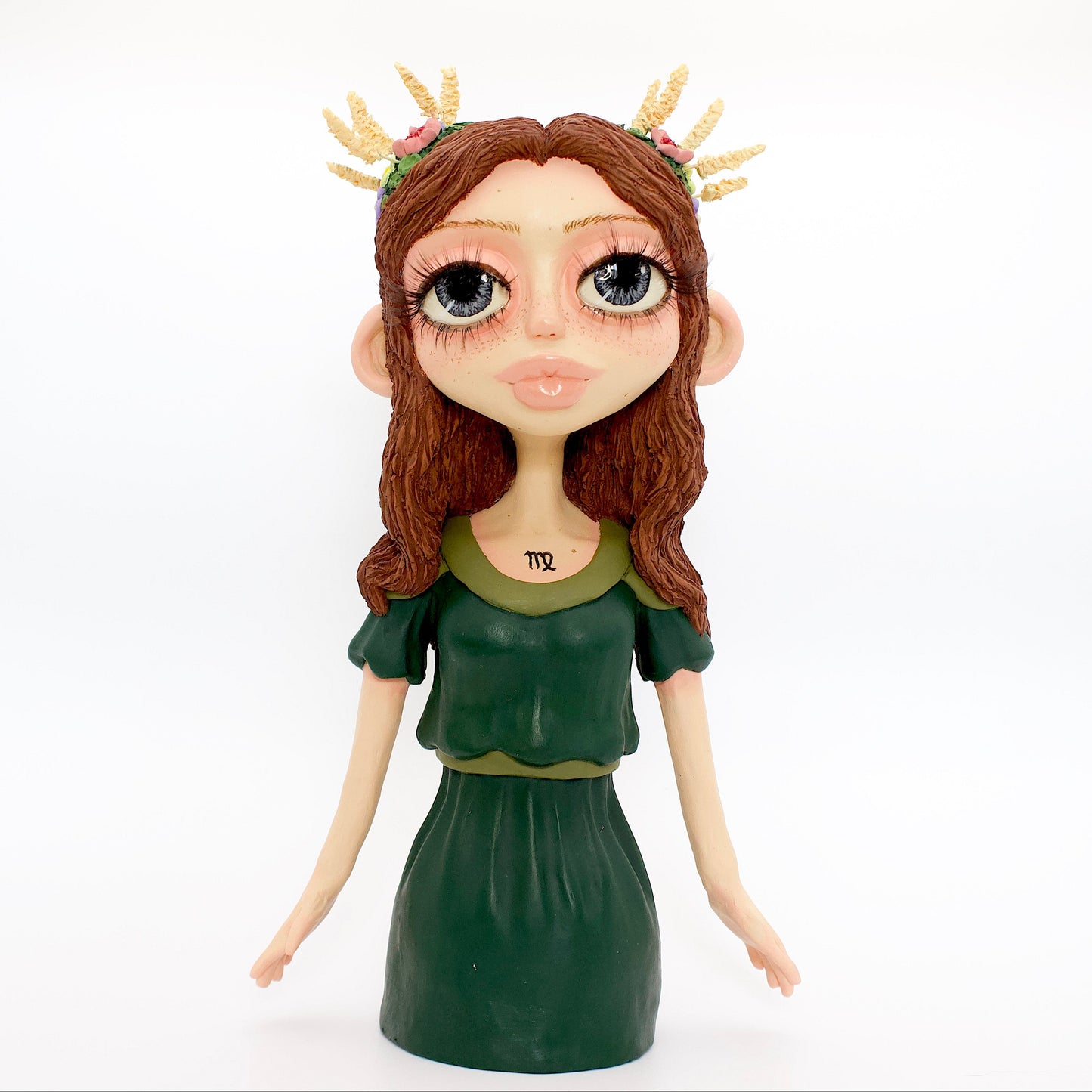 A polymer clay sculpture of the Virgo zodiac personified as a woman, featuring brown flowing hair, a forest green dress, and flowers and wheat in her hair.