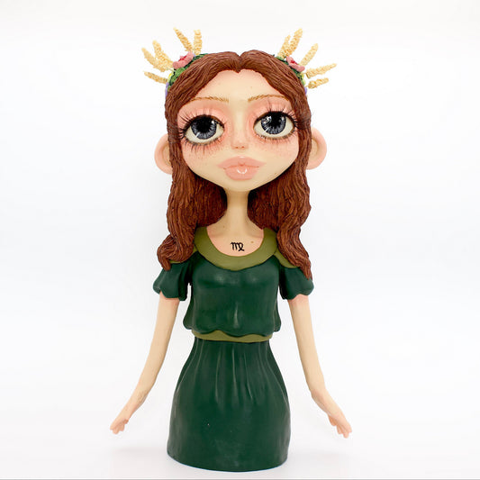 A polymer clay sculpture of the Virgo zodiac personified as a woman, featuring brown flowing hair, a forest green dress, and flowers and wheat in her hair.