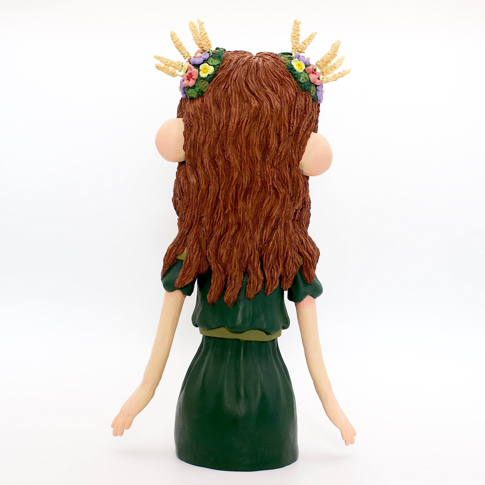A polymer clay sculpture of the Virgo zodiac personified as a woman, featuring brown flowing hair, a forest green dress, and flowers and wheat in her hair.